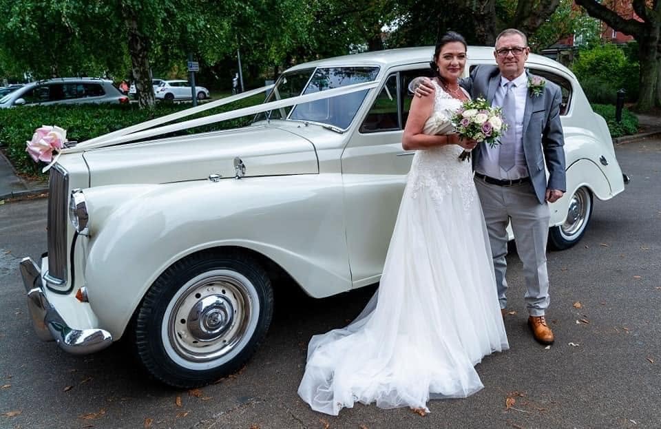 Bride and groom enjoying their wedding day beside a classic wedding car